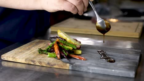 chef with spoon pouring tamari demi-glace beside the seared vegetables