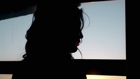 Silhouette-Einer-Lockigen-Dame-Am-Fenster-In-Einem-Dunklen-Raum