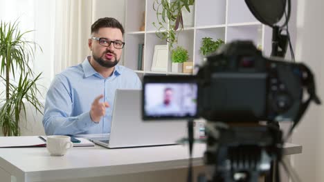 a male vlogger records video on a camera while sitting at a table at home. influencer filming a blog.