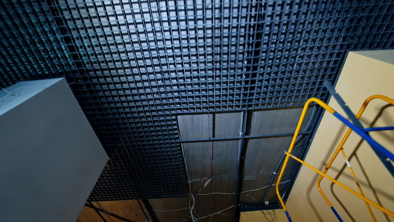 Dark ceiling with grate in the spacious premise. Unfinished room with air conditioner and wires. Low angle view.
