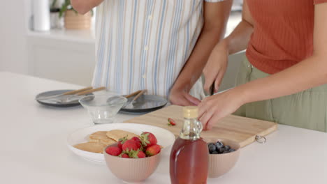 Slicing strawberries, diverse couple preparing breakfast together in modern kitchen, at home