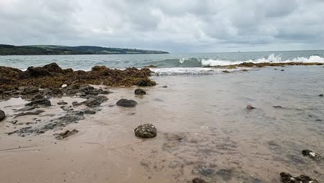 Slow-motion-ocean-waves-leaving-transparent-clear-water-over-sandy-Anglesey-beach-coastline