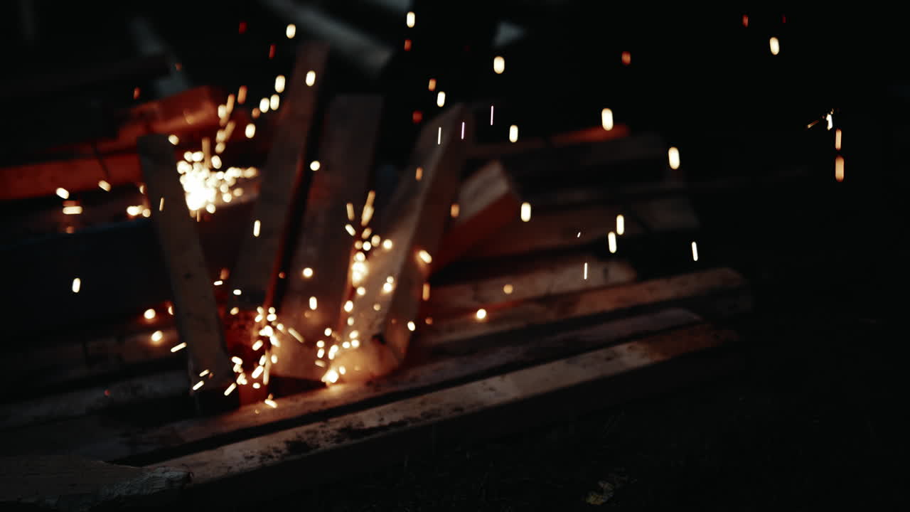 Orange glowing sparks fall onto some construction wood as the structure of a halfpipe is being welded