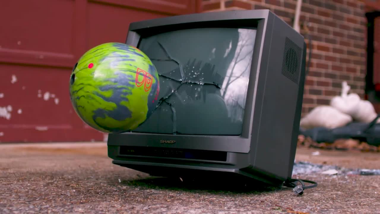 오래된 빈티지 검은 tv는 뒷면에 벽돌 벽과 금속 문과 함께 낮 동안 느린 동작으로 다채로운 파란색과 녹색 볼링 공으로 던집니다.