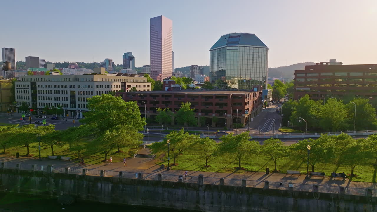 Beautiful twilight aerial of Portland, Oregon's Waterfront Park and west side. A cyclist rides down the bikepath. Wide shot, camera flies forward and pans right.