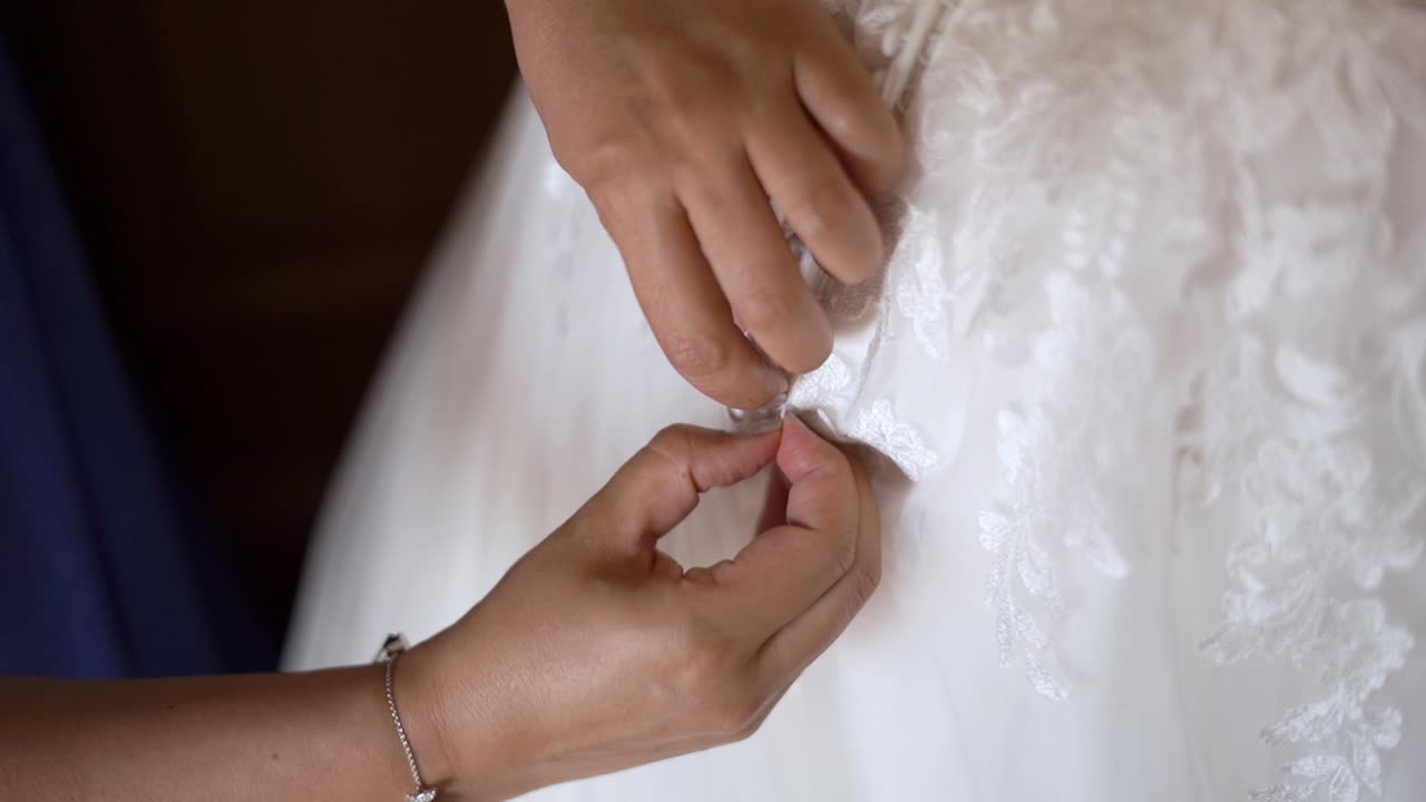 Detail shot of hands buttoning up a wedding white dress with silk details