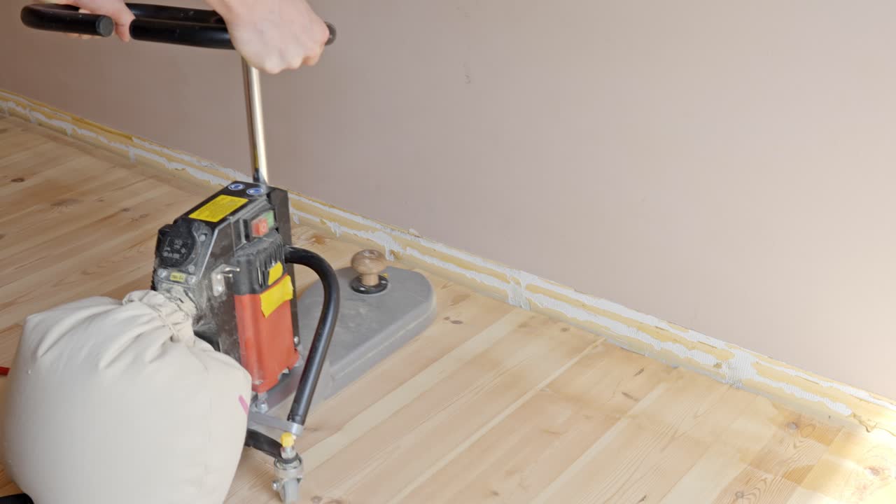 Fine sanding pass along wooden edge strip next to interior wall and corner, dust collection in bag