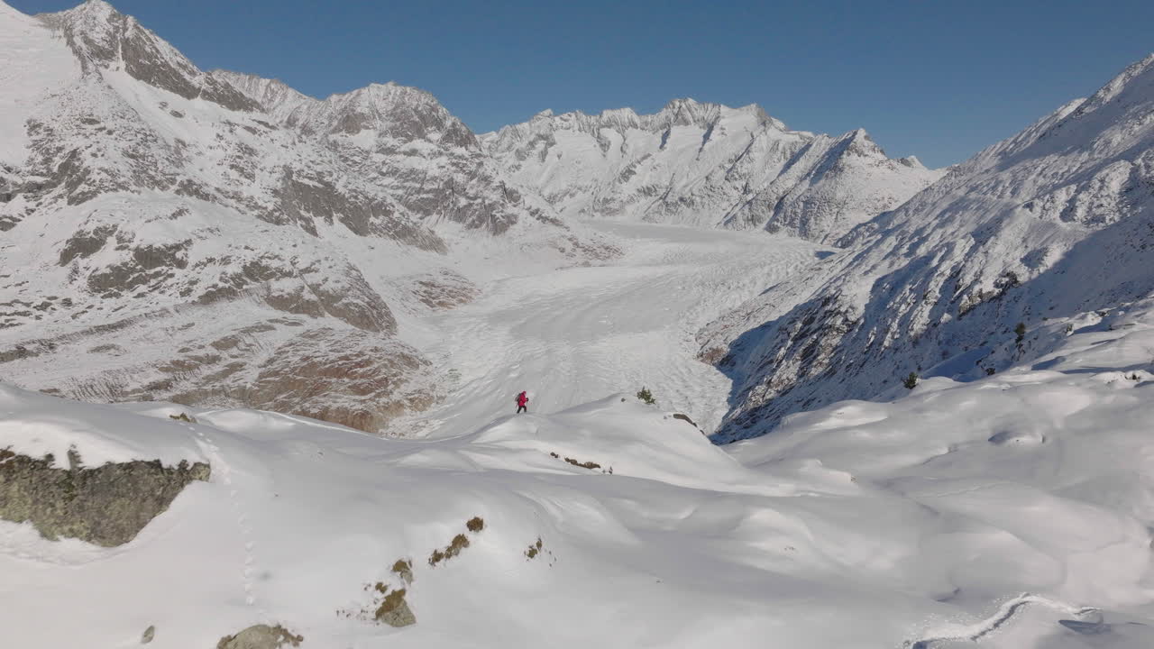 Ripresa aerea in Svizzera con una persona che cammina con le ciaspole in una giornata di sole con un ghiacciaio sullo sfondo.