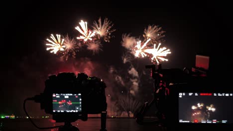 cameras lined up in a row in front of a pyrotechnic display at a beachfront during a fireworks festival