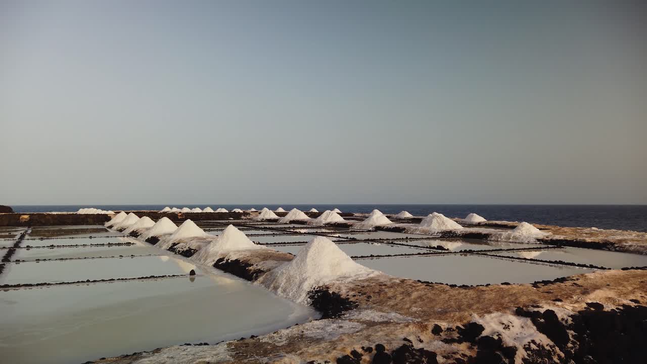 A lateral shot moving at ground level along a saltwork near the sea under a blue sky