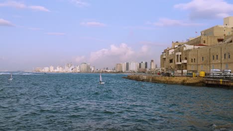 old jaffa city.old jaffa beach, tel aviv in the background' and a small sailing boat in the sea.an ancient and modern city.