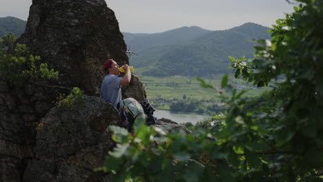 happy-smiling-man-drinking-bottle-of-water-from-a-thermos,-drinks-water,-Durnstein-castle-ruins-in-background,-mountain-valley-view,-friendly-Hydrating-male,-holiday-relaxation-trekking-hike-break