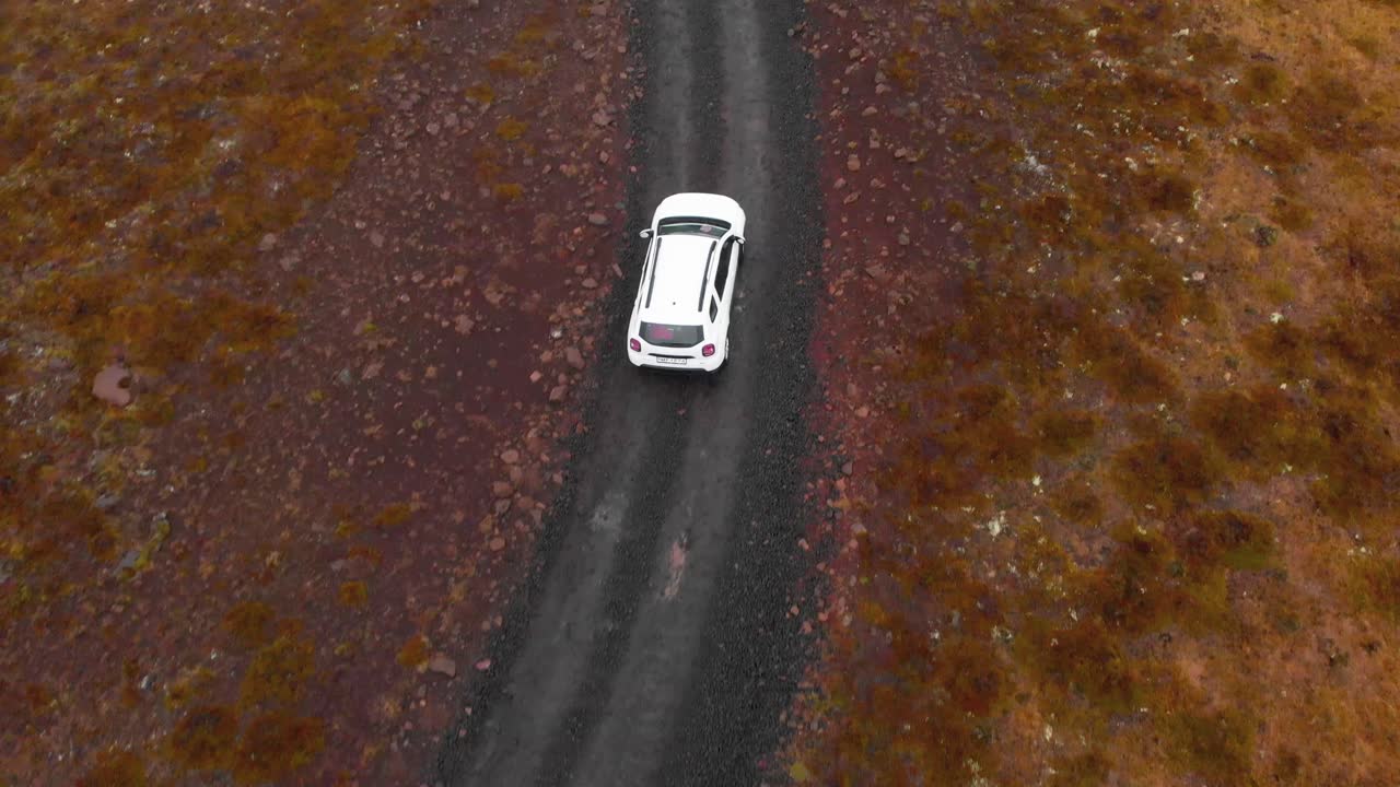 coche suv conduciendo lentamente por un camino de grava en un campo de brezo húmedo, islandia