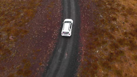 suv car driving slowly on gravel road in wet heath field, iceland