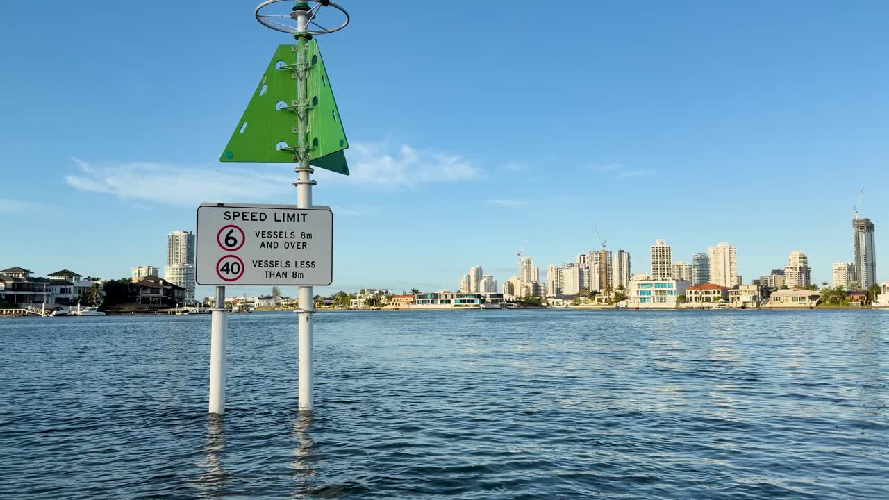 Floating buoy moves past waterway speed sign, city skyline in background, daylight, steady camera