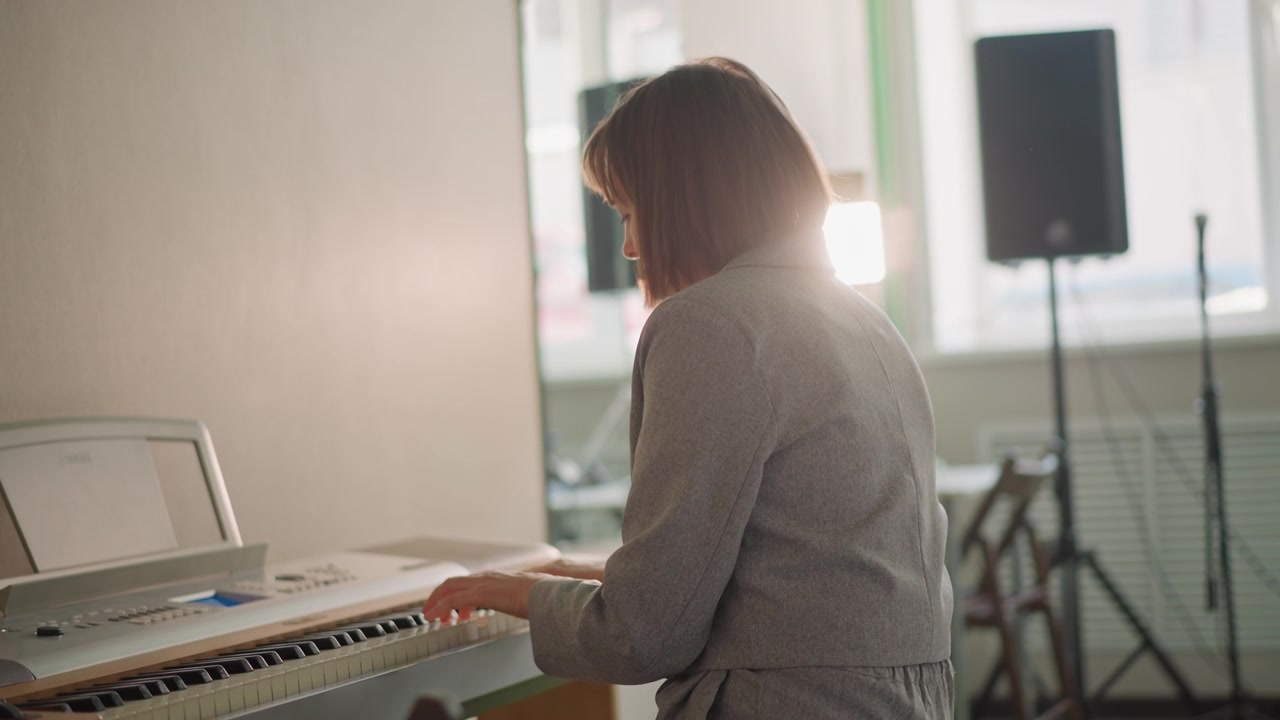 Pianista che suona la tastiera in studio, luce solare soffusa sui tasti e sull'altoparlante, insegnante che dimostra il fraseggio, postura concentrata e prova lenta, tempo calmo e atmosfera calda per la preparazione della lezione