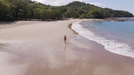 młoda piękna kobieta spacerująca samotnie po mokrym piasku w czarnym bikini w pięknej playa real w prowincji guanacaste