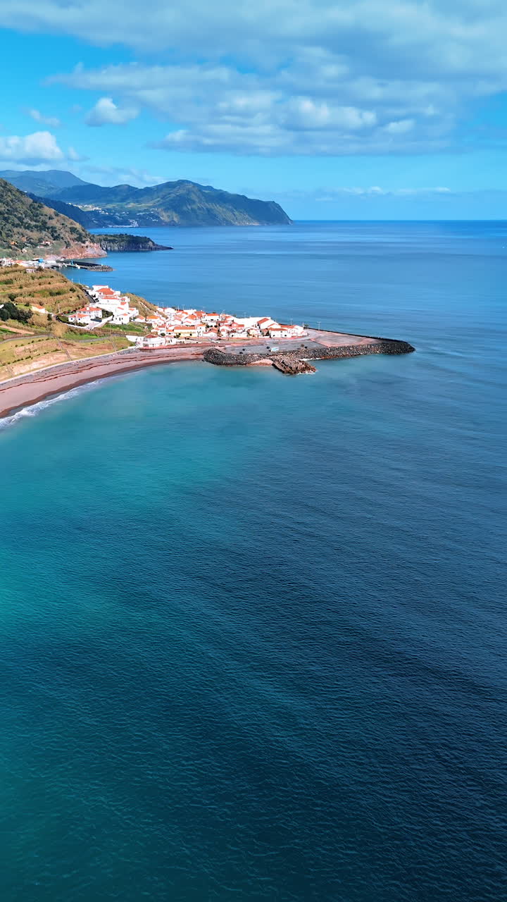 Approaching the village located on the coastline of the North Atlantic Ocean. Splendid scenery of the shore with rocks descending to the water. The Azorean Islands. Vertical video.