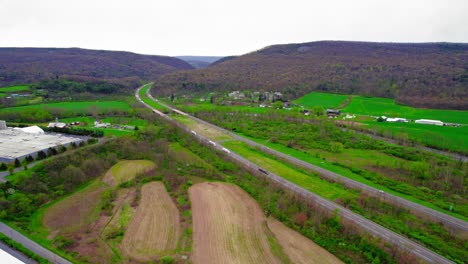 Orbiting-aerial-of-semi-trucks-navigating-through-Milesburg-PA-on-I-80-interstate,-vital-for-logistics-and-transport