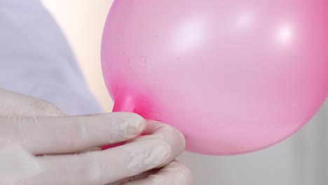close-up of gloved hands securing a pink balloon onto a glass bottle.