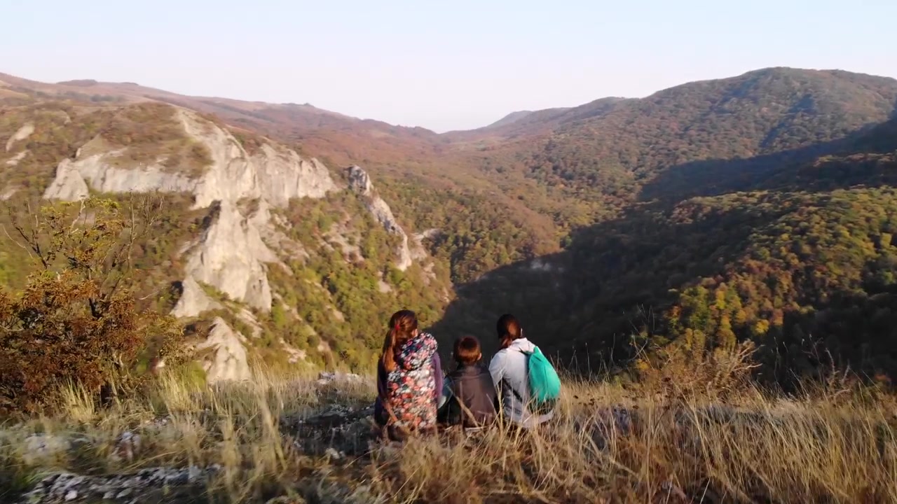 Ripresa orbitale di una madre e dei suoi figli seduti in cima a una collina che si godono il paesaggio.