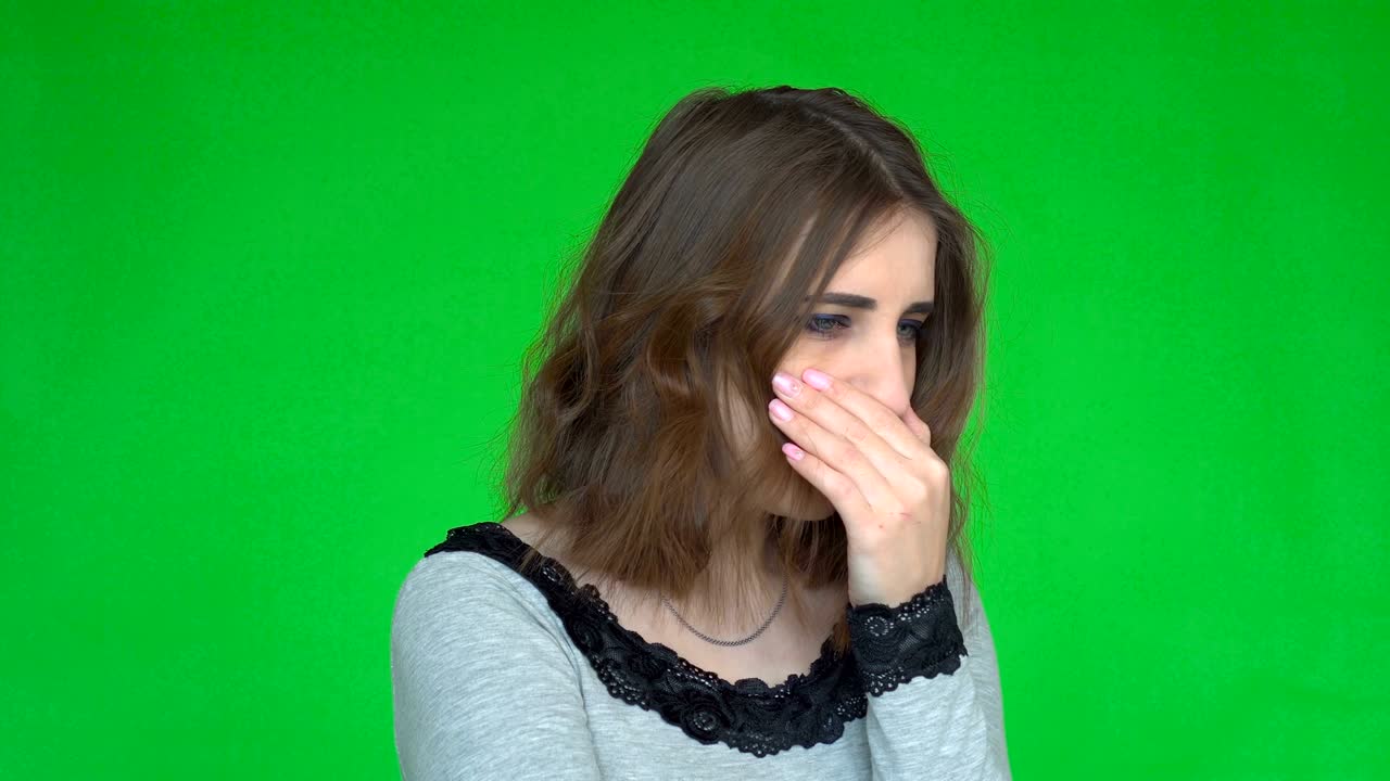 Young woman coughing with palm while looking at the camera over green background.