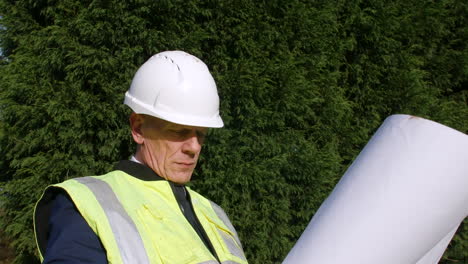 a construction manager architect standing in front of trees looking at plans and paperwork