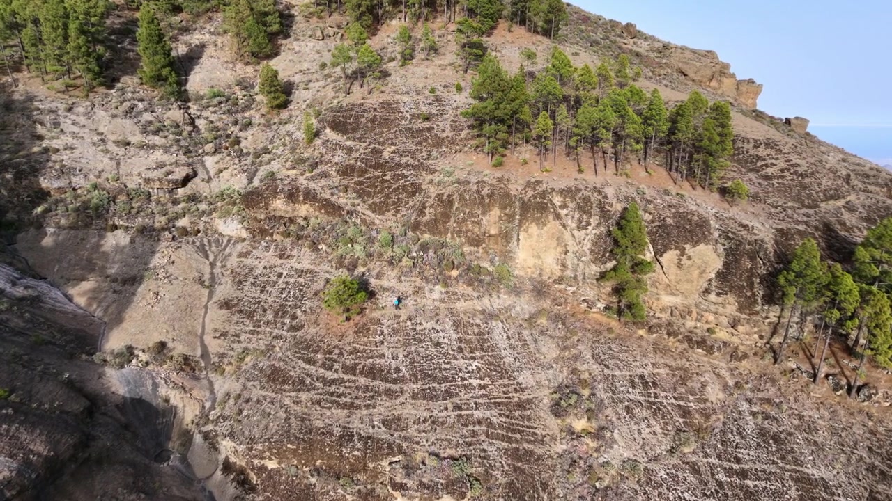 Aerial view of a lone person hiking across a rocky and arid mountain slope in Gran Canaria, Spain. Majestic volcanic landscape with trails