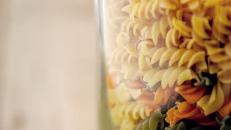 close-up of colored and original fusilli pasta in transparent jar glass