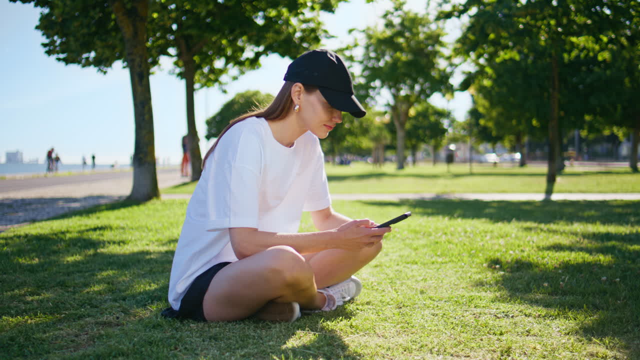 Calm lady reading sms sitting at green park grass. Relaxed brunette browsing