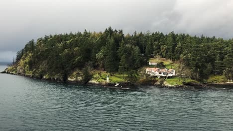 white house equipped with orange roof tiles and surrounded by green trees on a small island on a cloudy day while a small bird is flying over