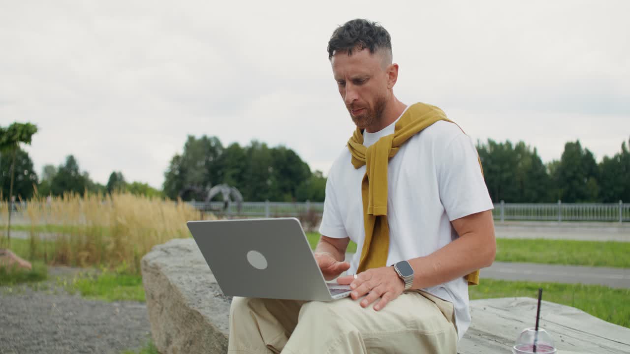 Man working on laptop and drinking beverage in the park