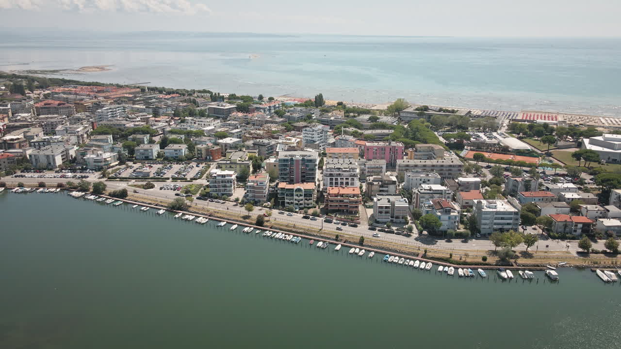 Smidig 4K UHD-drönare följer Grado stad till höger och visar bostadshus, en marina med båtar och den vidsträckta lagunen – perfekt för resefilmer, b-roll och stadslandskap.