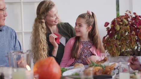 video of happy caucasian mother cleaning daughter's face at family dinner table