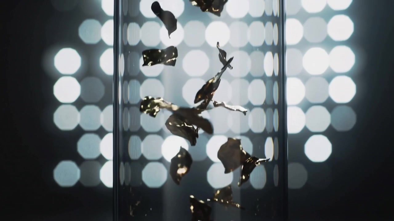 Air pulse lifting gold flakes, rising, tumbling inside clear cylinder on studio base with LED grid