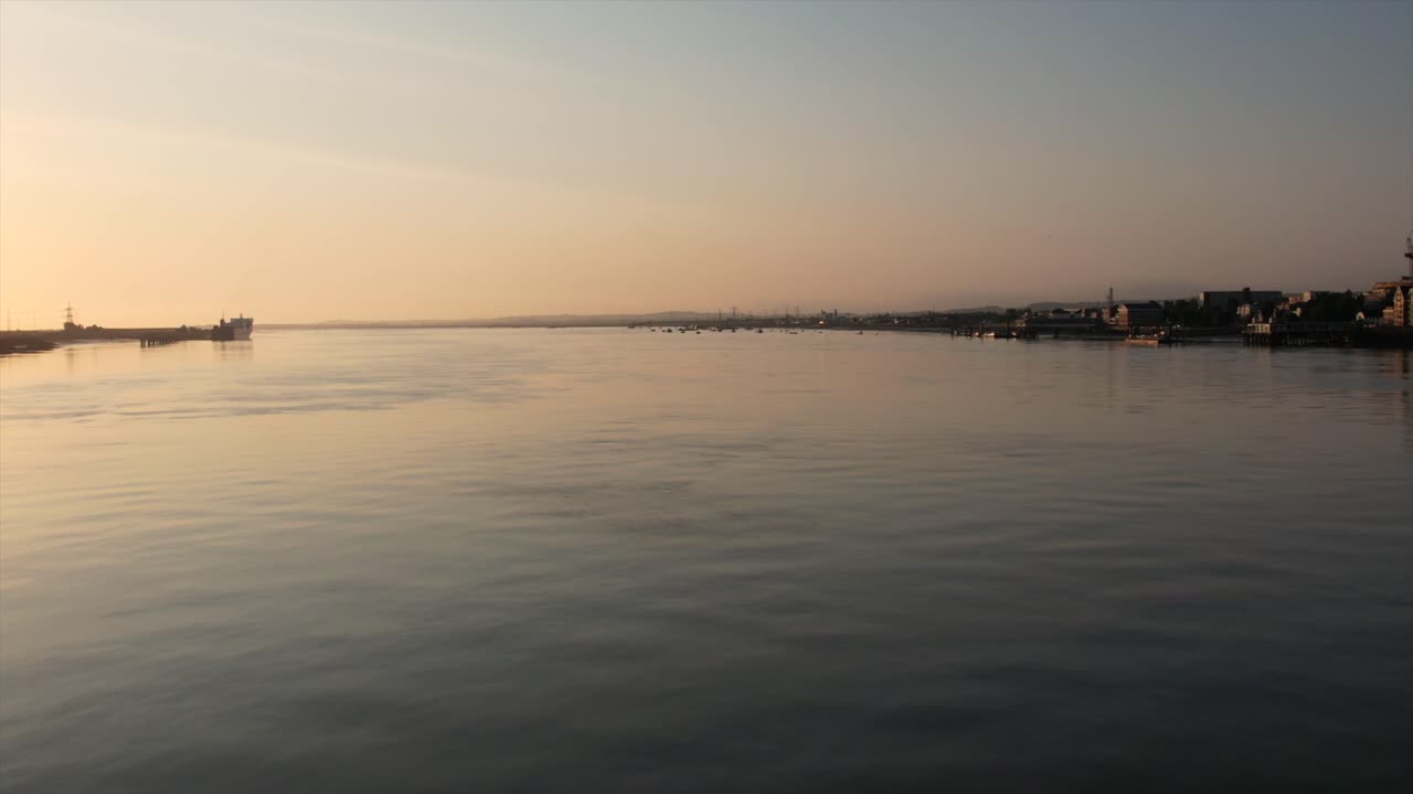 Sunset over Calm River with Boats and Distant Town