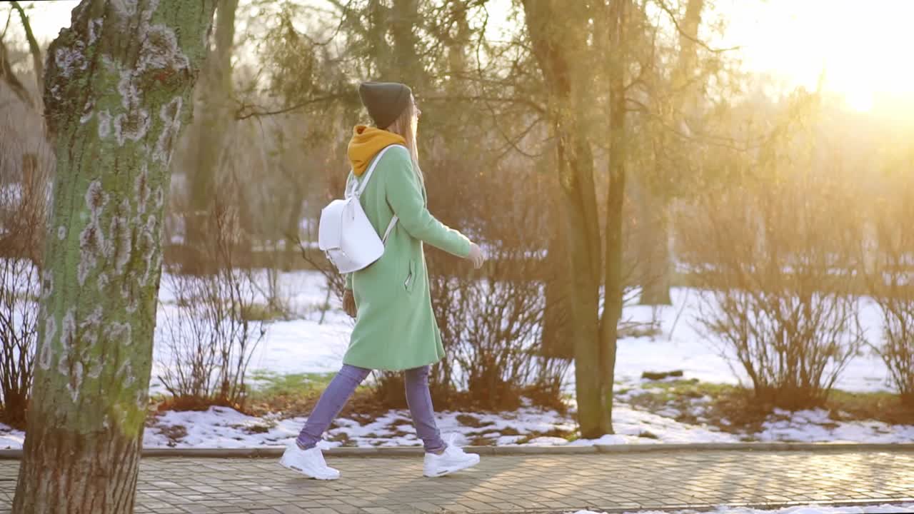 Woman walk freerly in winter park in green winter coat
