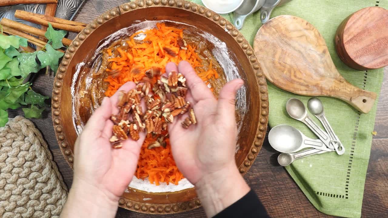 Baking a carrot cake loaf with cream cheese icing and topped with roasted salted pecans. Making a Autumn dessert with carrots, flour, sugar, nuts and frosting. Adding in the roasted pecans.