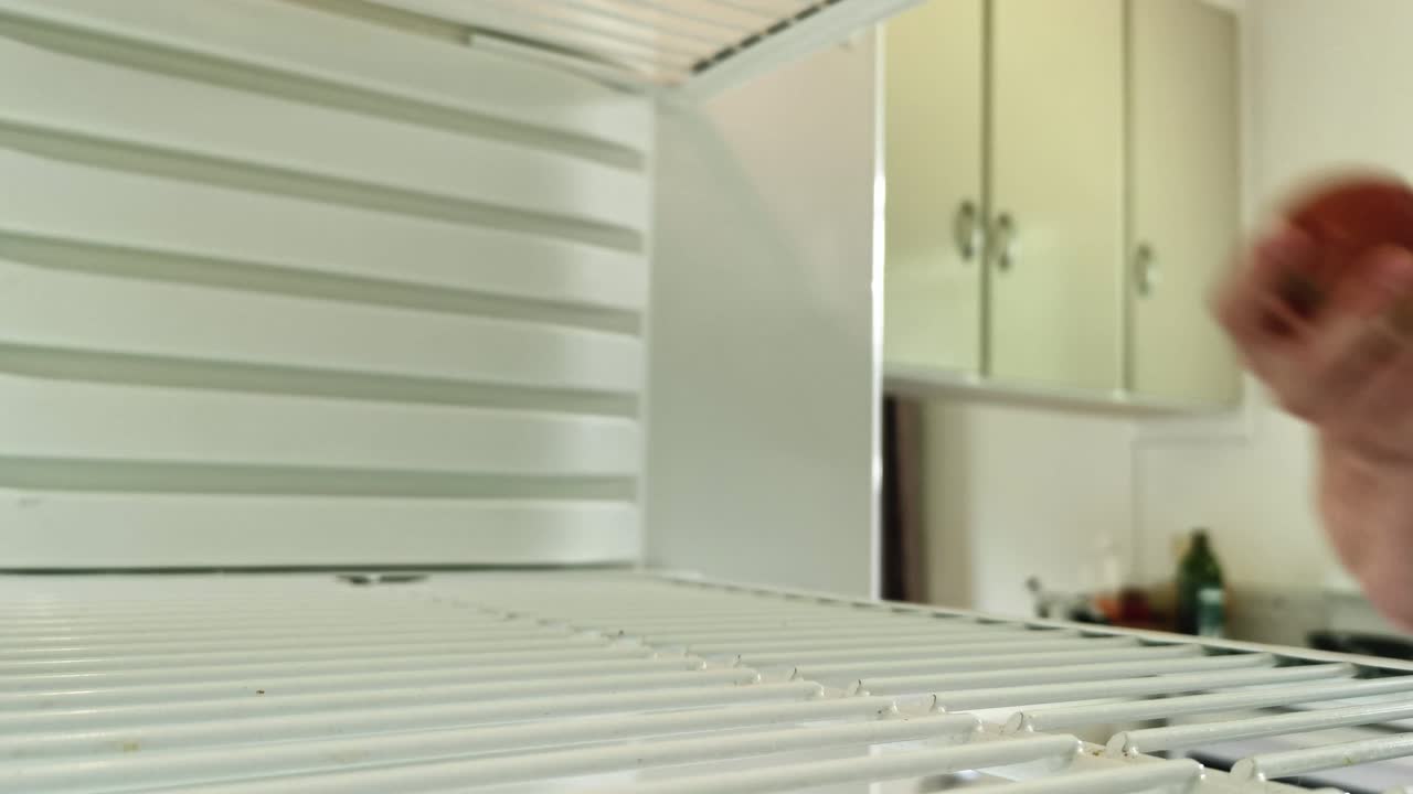 vista desde el interior del refrigerador del hombre alcanzando y agarrando la única manzana que queda