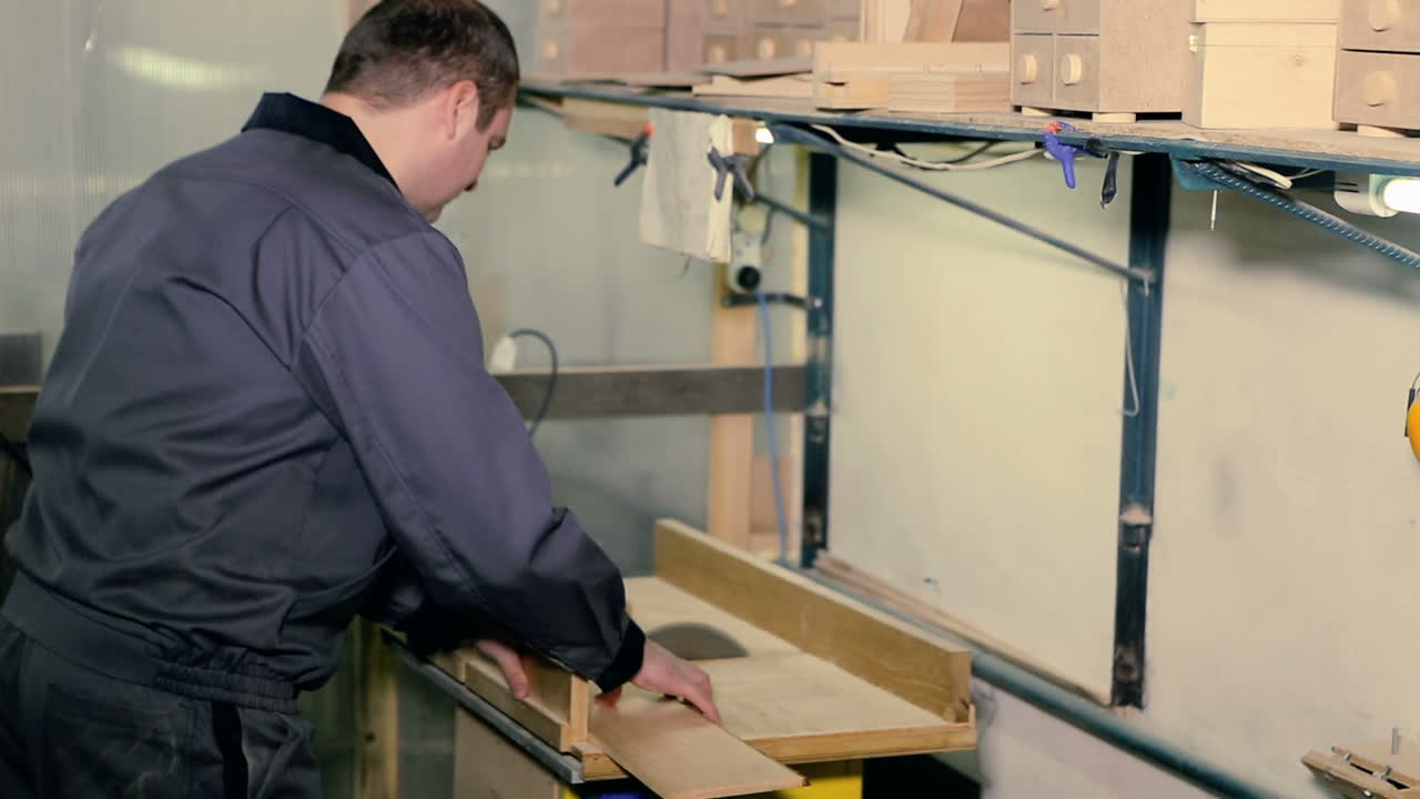 Carpenter is sawing a wooden plank with jig saw machine in carpentry workshop