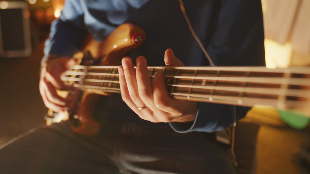 Primo piano statico di mani che pizzicano le corde di un basso elettrico in un accogliente studio