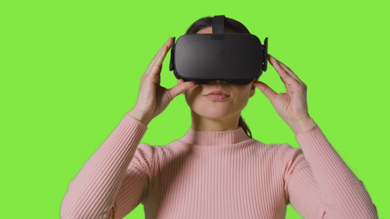 mujer poniendo auriculares de realidad virtual y mirando a su alrededor contra el fondo del estudio de pantalla verde
