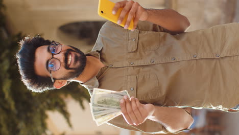 happy young man counting money dollar cash use smartphone calculator app in urban city street
