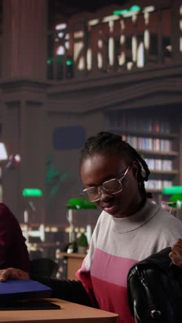 vertical video african american student comparing class notes with data from the library