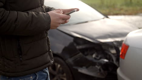 hombre enviando un mensaje de texto después de un accidente automovilístico en una carretera rural