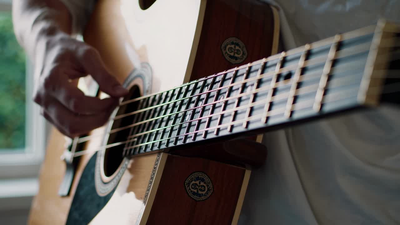 Primo piano video di una persona che strimpella una chitarra acustica, ripreso dal basso.