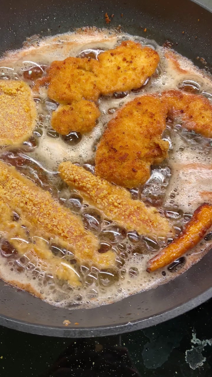 Chicken schnitzel fried sizzling in oil inside a pan on gas stove in a kitchen. Typical European dish cooking. POV of homemade cooked food. Preparing meal. UGC food chef foodie video reel social media