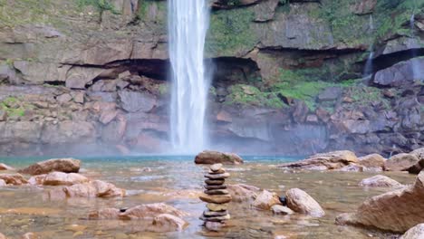 natural waterfall falling from mountain with pile of stones at day