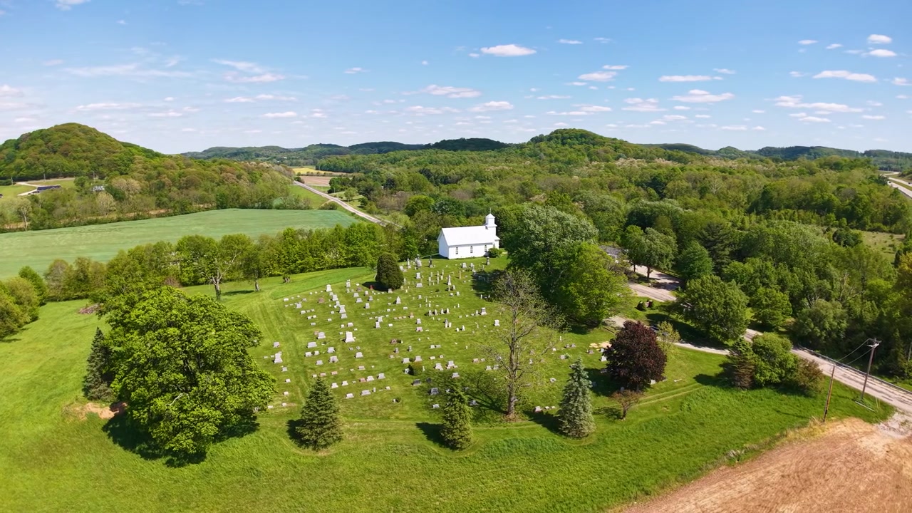 Aerial panorama of a white country church surrounded by orchard lawns and wooded hills