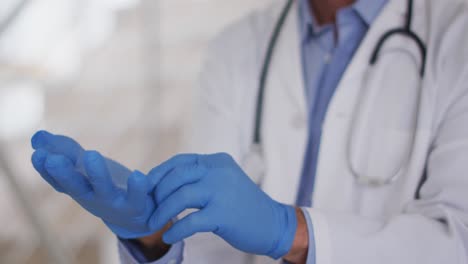 senior caucasian male doctor wearing face mask putting protective gloves on